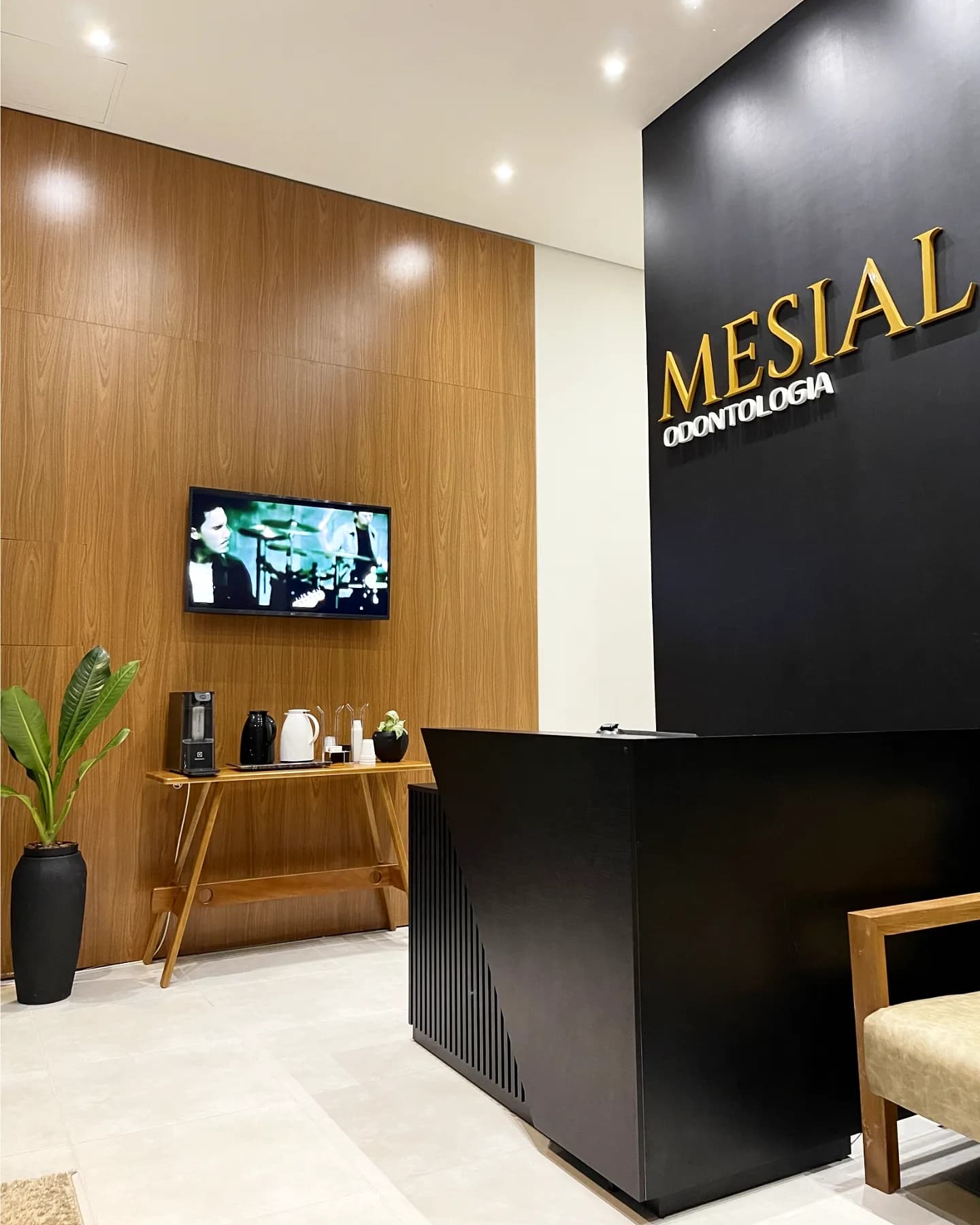 Recepção da Clínica Mesial, com painel de madeira, balcão de atendimento e cantinho do café