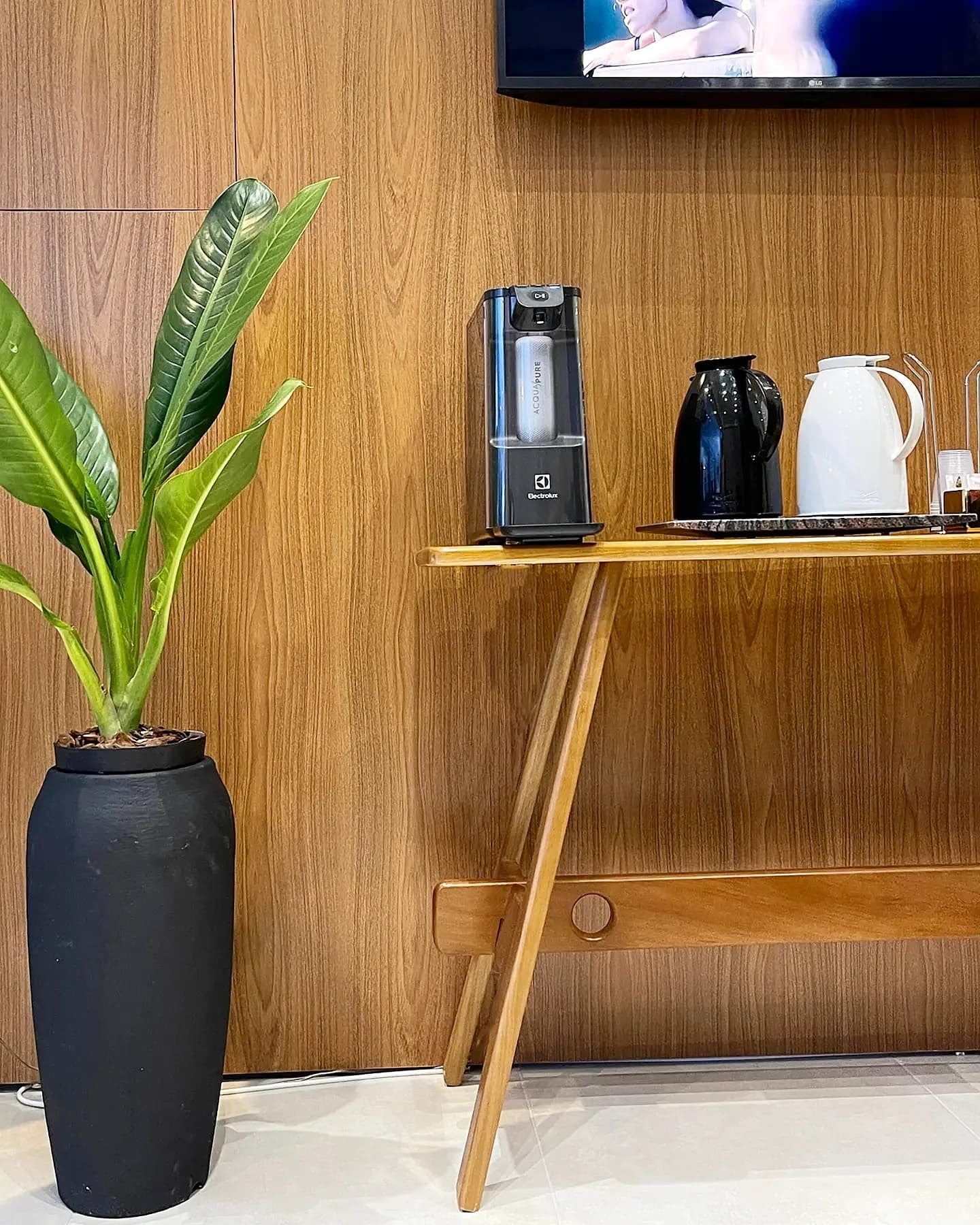 Cantinho do café na recepção da Clínica Mesial, com painel de madeira e planta